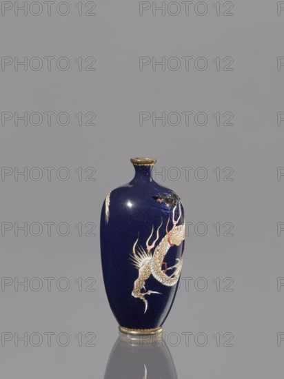 Vase, Japanese, Meiji period 1868–1912, cloisonné enamel, 19th/20th century; subject: Japanese dragon motif/dragons iconography; vessel; height 36.7 cm, diameter 4.6 cm;, A small glossy vase with a deep navy blue surface and gold rim details stands centered against a plain light gray background, showing a decorative depiction of a sinuous dragon in shades of cream, pale gold, white, and touches of red and black wrapping around its body, with additional gold and white accent motifs and a subtle reflection beneath the vase.