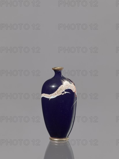 Vase, dragons iconography; Japanese art; Japanese dragon motif; Meiji 1868–1912; cloisonné enamel; 19th/20th century Meiji Period; Japan; vessel; height 9.5 cm; diameter 4.6 cm., A deep navy-blue ceramic vase with a narrow neck and flared rim sits upright against a plain light gray background, featuring a pale, sinuous dragon-like motif wrapping around its upper body in shades of white, cream, pale pink, and light blue, with small accents of red near the head; the rim and base have metallic gold tones, and the vase casts a soft reflection on the surface beneath it.