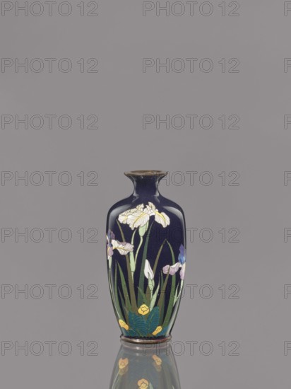 Vase, Ovoid vase with a short, thin, flared neck decorated with irises on a dark blue background. Cloisonné enamel. Meiji period, ca. 1900. Japan. Vessel. Height 9.1 cm; diameter 4.3 cm., A dark blue ceramic vase with a narrow neck and flared rim sits upright against a plain gray background, decorated with a painted floral design that includes a group of tall green leaves and stems and several white, purple, and blue flower blossoms, along with green foliage and small yellow flower accents near the base; the vase casts a subtle reflection on the glossy surface beneath it.