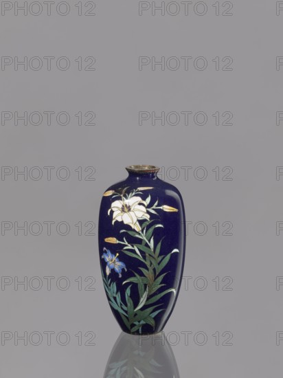 Vase, gift, repossession Krakow, lilies, Japanese art, Japanese, Meiji 1868–1912, cloisonné enamel, 19th/20th century Meiji period, Japan, vessel, height 9.1 cm, diameter 4.8 cm, A dark blue vase with a narrow neck and rounded shoulders sits against a plain gray background, decorated with painted white and blue flowers and green leaves, with small yellow buds and a light reflection visible on its glossy surface and a faint mirrored reflection beneath; colors visible include dark blue, white, blue, green, yellow, gray, and a hint of brown on the rim.