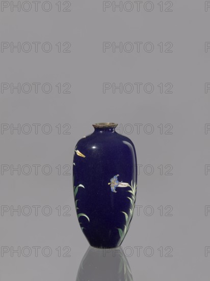 Vase, lilies; Japanese art; Japanese; Meiji 1868–1912; cloisonné enamel; 19th/20th century Meiji period; Japan; vessel; height 9.1 cm, diameter 4.8 cm, A tall oval vase with a deep blue glossy surface stands against a plain gray background; the vase has a narrow rim with a metallic-looking edge and is decorated with delicate floral motifs in green, pale yellow, and light blue, with leafy stems rising from the base and a small reflected image of the vase visible on the smooth surface beneath it.