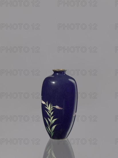 Vase, Meiji period 1868–1912, Japan; cloisonné enamel; 19th/20th century; vessel decorated with lilies; height 9.1 cm, diameter 4.8 cm., A dark blue glossy vase with a rounded, elongated shape and a small neck sits centered against a plain light gray background, showing a reflection on the surface beneath it; the vase features a painted plant motif with green leaves and a few pale purple and white flowers, and the rim has a metallic-looking band in a muted gold color.