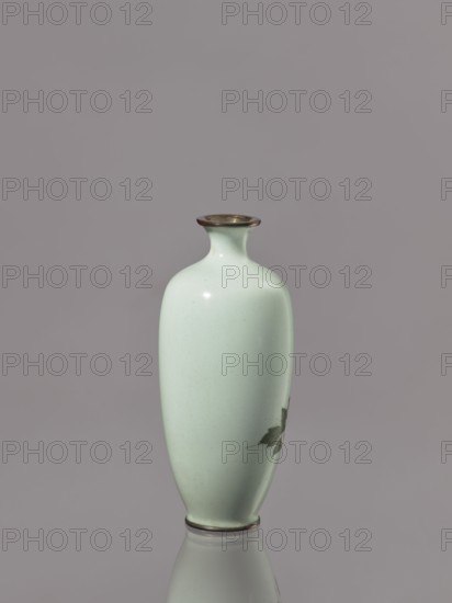 Vase, gift; repossession Kraków; Japanese; peonies; Meiji 1868–1912; cloisonné enamel; flowers iconography; symmetrical decoration; ca. 1900–1910; Japan; vessel; height 12.3 cm; diameter 5.3 cm, A pale green ceramic vase with a narrow neck, flared rim, and rounded body standing upright on a reflective surface, showing a small darker green leaf-like decoration on one side; the rim and base have a thin darker band, and the background is a muted grayish purple.