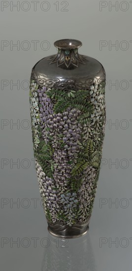 Vase, Hiratsuka, Mohei 1836-? maker. A slender ovoid, double-walled bottle on a very low ring foot with a narrow neck flaring at the spout. The outer wall is openwork and composed of densely arranged, colorfully enamaled cloisonné wisteria flowers and leaves, filling the entire surface of the vessel's body. The flowers are rendered naturalistically with clusters in shades of lilac and blue using multiple enamel tones; the leaves employ several green tones. In the lower part of the body, a strip of silver left around the foot is engraved with a stylized wave motif. The arms of the vessel are solid silver, with a strip of stylized clouds running above the floral ornament in a manner characteristic of Far Eastern art. The neck is enclosed by a rosette with petals decorated with a multicolored miniature stylized plant ornament featuring chrysanthemum half-rosettes, leafy forms, and volutes. Mark on the bottom: oval convex plaque with the artist's name: Hiratsuka. Ca. 1880–1890 Meiji Period...