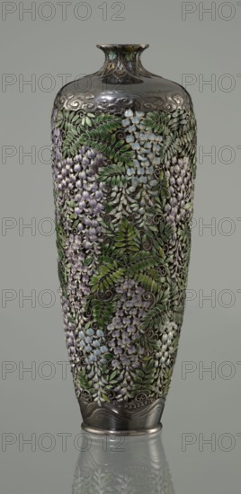 Vase, Hiratsuka, Mohei 1836-? creator, gift, Japanese art, Meiji 1868-1912. A slender ovoid, double-walled bottle on a very low ring foot with a narrow neck flaring at the spout. The outer wall is openwork composed of densely arranged, colorfully enameled cloisonné wisteria flowers and leaves filling the entire body. Flowers are rendered naturalistically in shades of lilac and blue using multiple enamel tones; leaves use several green tones. The lower body has a strip of silver left around the foot decorated with an engraved stylized wave motif. The arms of the vessel are solid silver, with a strip of stylized clouds above the floral ornament in a Far Eastern manner. The neck is enclosed by a rosette with petals decorated with a multicolored miniature stylized plant ornament with chrysanthemum half-rosettes, leafy forms, and volutes. Mark on the bottom: oval convex plaque with the artist's name: Hiratsuka. ca. 1880–1890 Meiji Period, Japan. Vessel; height 19.1 cm; diameter 7.2 cm., A t...