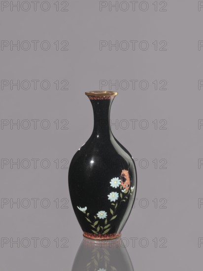 Vase, chrysanthemums, Japanese art, Japanese culture, flowers iconography, Meiji 1868–1912, cloisonné enamel, symmetrical decoration, ca. 1900, Japan, Nagoya, vessel; height 19.3 cm, diameter 9.1 cm, A glossy black vase with a narrow neck and flared rim stands against a muted gray background, featuring a decorative band of reddish accents at the rim and base, a painted floral motif of pale blue flowers with green leaves winding up one side, and a small reddish ornamental detail near the flowers; the vase casts a faint reflection on the surface below.