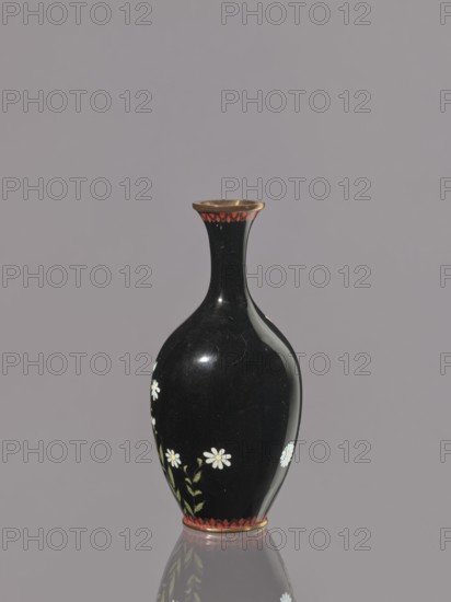 Vase, gift; repossession; chrysanthemums; Japanese art; Japanese culture; flowers iconography; Meiji 1868–1912; cloisonné enamel; symmetrical decoration; ca. 1900 Meiji Period, 1868–1912; Japan, Nagoya; vessel; height 19.3 cm; diameter 9.1 cm., A glossy black vase with a narrow neck and rounded body sits against a muted gray background, featuring small white daisy-like flowers with pale yellow centers and green leaves painted on its lower body, a band of red scalloped decoration near the base and rim, and a thin metallic-looking edge at the top, with the vase and its details reflected faintly on the surface beneath it.