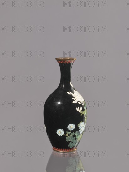 Vase, gift; repossession Krakow; chrysanthemums; Japanese art; Japanese culture; flowers iconography; Meiji 1868–1912; cloisonné enamel; symmetrical decoration; ca. 1900; Nagoya, Japan; vessel; height 19.3 cm; diameter 9.1 cm., A glossy black vase with a narrow neck and flared rim sits against a muted gray background; the vase features painted floral motifs in white and pale blue with green leaves, and has decorative red and gold accents near the rim and base, with a faint reflection visible on the surface below.