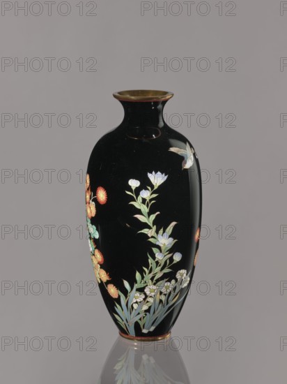 Vase; maker, gift; repossession Krakow; decorated with chrysanthemums and roses; Japanese, Meiji period ca. 1900; Nagoya, Japan; vessel; height 24.4 cm, diameter 11.7 cm., A tall black vase with a narrow neck and flared rim sits against a plain gray background, decorated with painted floral motifs in colors including white, pale blue, green, red, orange, and yellow, and showing a small bird in shades of white and pale brown near the upper side; the vase has a subtle reflective sheen and a thin metallic rim at the top and base, and a soft reflection of the vase appears on the surface below.