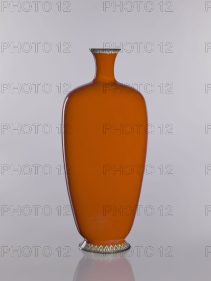 Vase, cloisonné enamel; Japanese, Nagoya; Meiji–Taisho period, ca. 1910–1920; height 24.0 cm, width 10.4 cm, depth 8.5 cm. Decoration: chrysanthemums, cherries, birds, flowers; function: decorative vessel., An orange vase with a narrow neck and flared rim sits centered against a pale gray background; the vase has a smooth glossy surface and a slightly tapered, rounded body, with a decorative band of pale green and off-white scalloped shapes around the rim and base, and a small reflected shadow beneath it.