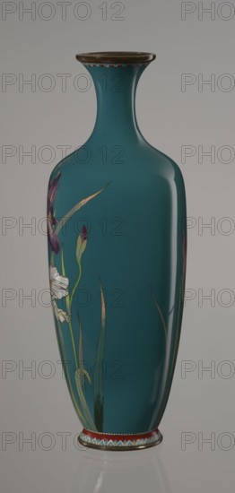 Vase, gift, repossession Krakow — Ovoid vase one of a pair, slender, on a low ring-shaped foot and a narrow neck, flaring at the rim. The foot and mouth are framed with sheet metal. Decorated with a motif of a blooming iris bush rendered naturalistically with varied color tones. Executed using the yusen cloisonné enamel technique against a uniform sea-green background. Around the foot and rim are narrow, colorful yusen borders composed of small triangular forms called cicada wings. Japanese, Meiji period, ca. 1900; Nagoya. Vessel; height 25 cm, width 9.7 cm, depth 8.8 cm., A tall, slender vase with a narrow neck and flared rim sits against a neutral background, the main body covered in a deep teal color with a glossy finish; decorative floral motifs appear on one side featuring elongated green leaves and buds, a few purple petals, and a white flower with pale detailing, while the rim and base have narrow bands with small scalloped and geometric accents in colors including red, blue, wh...