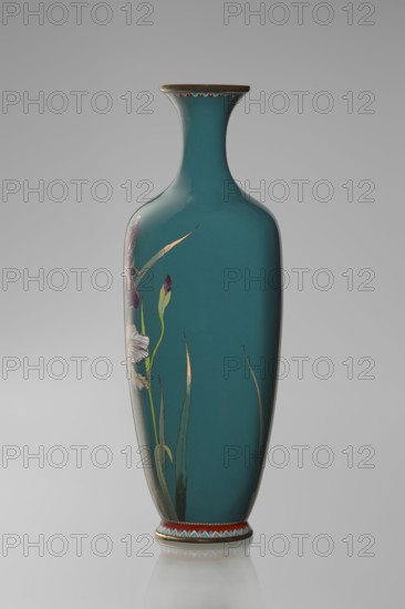 Vase, ovoid one of a pair, slender on a low ring-shaped foot with a narrow neck flaring at the rim; foot and mouth framed with sheet metal. Decorated with a naturalistic blooming iris bush in a variety of color tones, executed using the yusen cloisonné enamel technique against a uniform sea-green background. Narrow colorful borders of small triangular cicada wing forms around the foot and rim. Cloisonné enamel, ca. 1900 Meiji period, 1868–1912. Japan, Nagoya. Vessel. Height 25 cm; width 9.7 cm; depth 8.8 cm., A tall, slender vase with a narrow neck and flared rim, shown against a neutral gray background, finished in a deep teal color with a glossy surface; one side of the vase features a painted botanical motif with long green leaves and a few flower buds and blossoms in shades of white, purple, and pale yellow; the rim and base have decorative bands incorporating colors such as gold, red, blue, and white; soft reflections appear on the vase surface and on the surface beneath it.