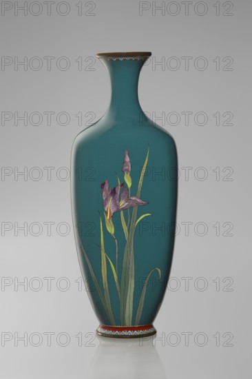 Vase, gift, repossession Krakow — irises — Japanese art, Meiji 1868–1912 — flowers iconography — cloisonné enamel — Japanese culture — Ovoid vase one of a pair, slender, on a low ring-shaped foot and a narrow neck, flaring at the rim. The foot and mouth are framed with sheet metal. Decorated with a motif of a blooming iris bush, captured with naturalistic fidelity and attention to a variety of color tones. Executed using the yusen technique, the motif is placed against a uniform sea-green background. Around the foot and the rim there are narrow, colorful borders, also made using the yusen technique, composed of small triangular forms called cicada wings. Ca. 1900 Meiji Period, 1868–1912, Nagoya, Japan. Vessel. Height 25 cm; width 9.7 cm; depth 8.8 cm., A tall, slender vase with a narrow neck and flared rim sits against a pale gray background, the vase surface a deep teal color with a glossy finish; a stylized floral motif decorates the front, showing a purple flower with lighter purple...