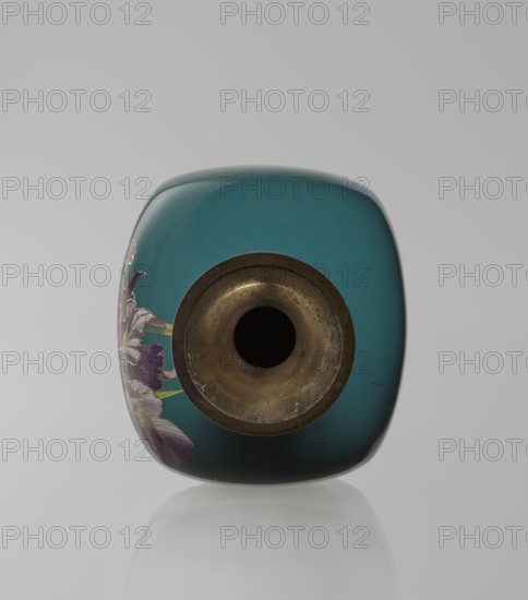 Vase, Ovoid vase one of a pair, slender, on a low ring-shaped foot with a narrow neck flaring at the rim; foot and mouth framed with sheet metal. Decorated with a motif of a blooming iris bush rendered with naturalistic fidelity and varied color tones, executed using the yusen cloisonné enamel technique against a uniform sea-green background. Around the foot and rim are narrow, colorful yusen borders composed of small triangular forms called cicada wings. Meiji period, ca. 1900. Japan, Nagoya. Cloisonné enamel. Vessel; height 25 cm, width 9.7 cm, depth 8.8 cm., The image shows the top view of a rounded square vase with a glossy teal surface and a circular metal rim around a dark central opening; a floral design with purple and white petals and green stems is partially visible on one side, and the metal rim appears aged with brownish and bronze tones; the background is a smooth light gray and the vase casts a soft, faint reflection below.