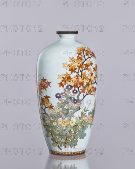 Vase, cloisonné enamel, chrysanthemums and maples, plant ornaments; Ovoid elongated vase with narrow spout; Japanese, Nagoya; Meiji–Taisho period, ca. 1910–1920; height 12.4 cm, diameter 16.3 cm., A pale blue ceramic vase with a narrow neck and rounded shoulder stands against a light gray background, decorated with a painted scene of a tree bearing orange and yellow leaves and a grouping of flowering plants at its base; the flowers include purple, yellow, and white blossoms with green foliage, and the tree branches and flower stems are outlined in dark brown, while the vase rim and base feature a band of brown tones.