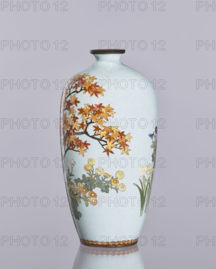 Vase, cloisonné enamel, ovoid vase elongated with a narrow spout, decorated with chrysanthemums and maples plant ornaments, flowers iconography. Japanese, Nagoya; Meiji 1868–1912/Taisho 1912–1926, ca. 1910–1920. Vessel; height 12.4 cm, diameter 16.3 cm., A tall ceramic vase with a pale bluish-white surface, featuring a painted design of a tree branch with autumnal leaves in shades of orange, red, and yellow, a group of small flowers in yellow and pale pink with green-gray foliage, and a few green leaves and stems; the vase has a narrow neck with a dark brown rim and a decorative band in warm brown tones around the base, all set against a soft light gray background.