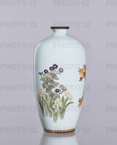 Vase, chrysanthemum and maple decoration in cloisonné enamel, ovoid elongated vase with narrow spout, Japanese Meiji/Taisho period, ca. 1910–1920, Nagoya, Japan; height 12.4 cm, diameter 16.3 cm; decorative vessel, flowers iconography., A pale blue ceramic vase with a narrow neck and dark brown rim stands against a light lavender background, decorated with painted floral clusters including purple, white, yellow, and orange blossoms with green leaves, and a decorative band of alternating brown and gold shapes near the base, the vase resting on a reflective surface that shows a faint mirrored outline.
