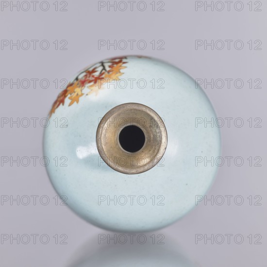 Vase, cloisonné enamel, chrysanthemums and maples, plant ornament; ovoid elongated vase with narrow spout., Japan, Nagoya. Meiji–Taisho period, ca. 1910–1920. Height 12.4 cm; diameter 16.3 cm., A round ceramic vessel shown from above with a smooth pale blue surface, a central circular metallic rim with a dark interior, and a decorative cluster of autumn-colored leaves in shades of orange, red, and yellow near the edge, all against a soft light gray background.