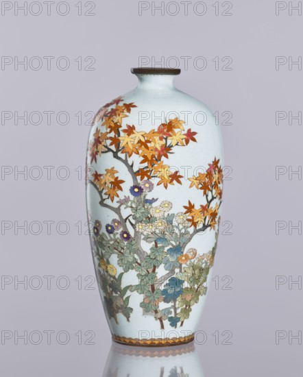 Vase, cloisonné enamel; ovoid vase, elongated with a narrow spout; decorated with chrysanthemums and maples, plant ornaments and flowers iconography; Japanese art; Meiji/Taisho period, ca. 1910–1920; Nagoya, Japan; height 12.4 cm, diameter 16.3 cm., A tall, rounded ceramic vase with a narrow neck and a dark rim, shown against a pale gray background, decorated with a painted scene of tree branches and foliage; the leaves on the upper branches are shades of orange, red, and yellow, and lower foliage includes greens, blues, and muted browns with clusters of flowers in purple, white, yellow, and pale blue, all outlined in darker tones, and a patterned band of warm brown and yellow hues encircles the base.