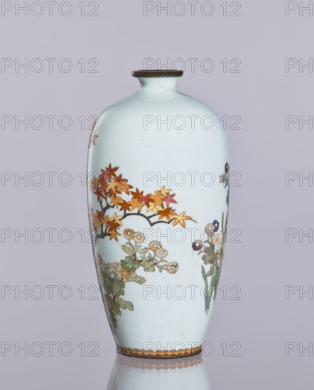 Vase, cloisonné enamel, ovoid elongated form with a narrow spout, decorated with chrysanthemums, maples, and other plant ornaments; Japanese, Nagoya; maker, Meiji–Taisho period, ca. 1910–1920; height 12.4 cm, diameter 16.3 cm., A pale bluish-white ceramic vase with a narrow neck and small rounded rim sits against a muted lavender-gray background, decorated with painted floral and foliage motifs including a branch with orange and reddish maple-like leaves, clusters of small daisy-like flowers in light cream and pale green leaves, and a few taller slender green leaves with small purple-centered blossoms; the rim has a thin darker band and the base edge shows a scalloped decorative border in shades of brown, orange, and gold.