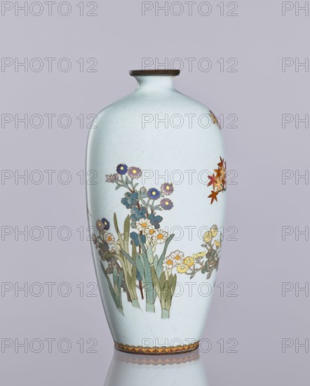 Vase, cloisonné enamel; ovoid vase, elongated with a narrow spout; chrysanthemums and maples decoration; plant ornaments, flowers iconography; Japanese art, decorative vessel; Taisho 1912–1926 / Meiji 1868–1912, ca. 1910–1920; Nagoya, Japan; height 12.4 cm, diameter 16.3 cm., A pale bluish vase with a narrow neck and dark brown rim stands upright against a soft gray-lavender background, decorated with a painted scene of flowering plants including leaves in shades of green and bluish-green and blossoms in purple, blue, yellow, white, and orange, with a band of alternating warm tones around the base and a soft reflection visible on the surface beneath it.