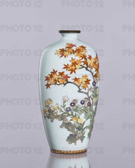 Vase, cloisonné enamel, ovoid elongated vase with a narrow spout; decoration: chrysanthemums, maples, and plant ornaments flowers iconography; Japanese art, Meiji 1868–1912 / Taisho 1912–1926, ca. 1910–1920; maker, Nagoya, Japan; height 12.4 cm, diameter 16.3 cm., A tall, slender vase with a pale bluish-white background featuring painted branches with autumnal leaves in shades of orange, red, and yellow, and a lower cluster of flowers and foliage in greens with blooms in purple, yellow, and pale pink; the vase has a narrow neck with a dark brown rim and a decorative band near the base in brown and golden tones, all shown against a muted light gray-lavender background.