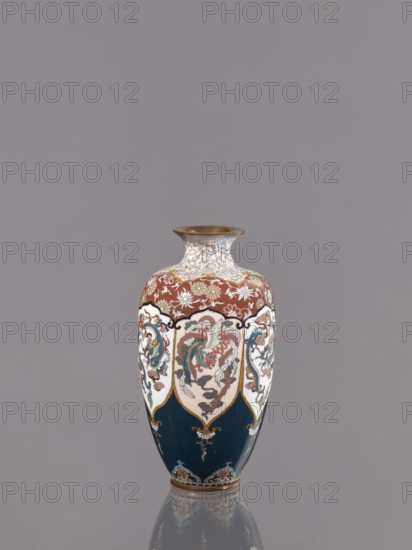 Vase, gift, repossession — phoenixes iconography, plant ornament, dragons iconography; Japanese art, Japanese culture; Japanese dragon motif, hoo phoenix; Meiji 1868–1912; cloisonné enamel. Description: Vase on a small ring-shaped foot with a short neck ending in a spout widening toward the top. Decoration: stylized plant ornament in six reserves alternating dragon and phoenix. Date: ca. 1890–1900 Meiji period. Place of origin: Kyoto, Japan. Medium: cloisonné enamel. Dimensions: height 15.0 cm; diameter 8.0 cm., A decorative vase with a rounded body and narrow neck sits against a plain gray background; its colors include deep blue, rusty red, white, gold, teal, and touches of black and brown, with ornate painted panels showing stylized birds and floral motifs in shades of teal, red, and cream, gold outlining and accents, a band of floral pattern near the shoulder in cream and gold against a red field, and a gold rim at the mouth, with a subtle reflection of the vase visible on the surf...