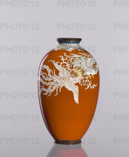 Vase, cloisonné enamel, phoenixes iconography, Japanese art, vases, Japanese culture, plant ornaments, decorative vessel, Meiji 1868-1912, Taisho 1912-1926, dark brick-red background of decoration, ca. 1910–1920, Japan; vessel; height 12.8 cm, diameter 7.7 cm, An oval-shaped vase with a glossy orange surface sits against a pale gray background; the vase features an ornate white and pale gray bird design with flowing feather and cloud-like motifs wrapping around its upper half, a dark rim at the top with a hint of blue decoration beneath it, and a dark base whose reflection appears faintly on the surface below.
