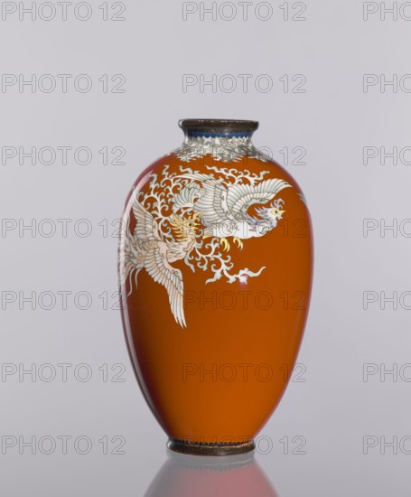 Vase, cloisonné enamel, phoenixes iconography, Japanese art, vases, plant ornaments, Meiji 1868–1912, Taisho 1912–1926, dark brick-red background of decoration, ca. 1910–1920, Japan; vessel; height 12.8 cm, diameter 7.7 cm, A smooth, glossy vase in a rich orange color with a rounded, tapered shape and a narrow dark rim at the top and a matching dark base, decorated with a group of pale, intricately detailed birds with flowing feathers and stylized swirling motifs in light cream and white tones, set against the orange surface, with small areas of blue near the top rim and subtle reflections on the vase and the pale gray background.