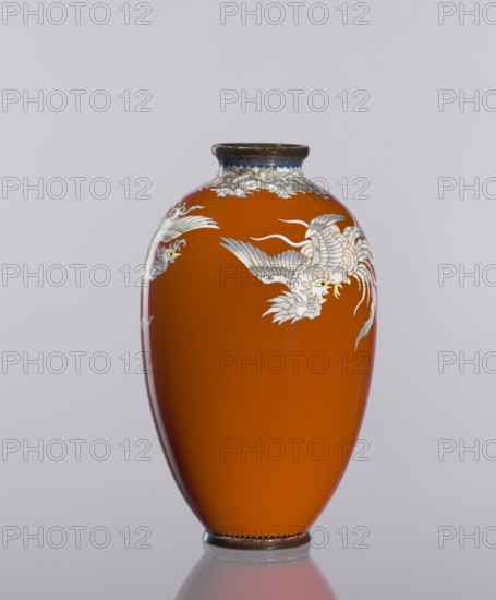 Vase, cloisonné enamel, phoenixes iconography, Japanese art, vases, plant ornaments, Meiji 1868-1912, Taisho 1912-1926, dark brick-red background of decoration, ca. 1910–1920 Meiji/Taisho periods, Japan, vessel; height 12.8 cm, diameter 7.7 cm., A smooth orange vase with a rounded, elongated shape and a narrow neck, decorated with white and gray stylized bird motifs and cloudlike patterns near the top, a dark rim at the mouth, and a dark base that reflects faintly on the surface below; visible colors include orange, white, gray, dark brown, and a hint of yellow in the bird details, set against a pale neutral background.