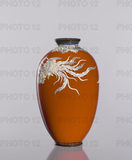 Vase, cloisonné enamel, phoenixes and plant ornaments, dark brick-red background of decoration, ca. 1910–1920 Meiji/Taisho periods, Japan; vessel; height 12.8 cm, diameter 7.7 cm; Meiji 1868–1912, Taisho 1912–1926., A smooth, glossy vase in a rich orange color stands upright against a pale gray background, featuring a decorative bird-like motif in white and light gray with delicate flowing tail feathers and a small yellow accent near its head, a band of white and blue ornamental detailing near the narrow dark rim, and a dark base with a subtle reflective surface beneath it.