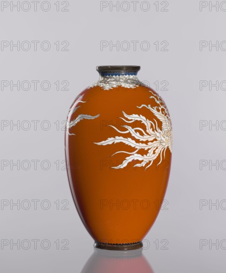Vase, cloisonné enamel, phoenixes and plant ornaments, dark brick-red background of decoration, Japanese, Meiji 1868–1912/Taisho 1912–1926, ca. 1910–1920, vessel, height 12.8 cm, diameter 7.7 cm., An orange vase with a glossy finish sits against a pale gray background, displaying a decorative white, flowing organic pattern on its curved surface; the neck rim and base have dark metallic accents with a hint of blue near the top rim, and the vase casts a faint reflection on the surface beneath it.