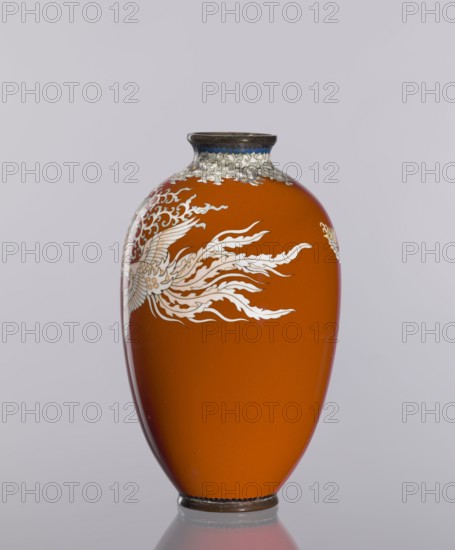 Vase, cloisonné enamel, decorated with phoenixes and plant ornaments on a dark brick-red background; Japanese, Meiji–Taisho period, ca. 1910–1920; vessel; height 12.8 cm, diameter 7.7 cm., An orange vase with a rounded, elongated shape sits against a pale gray background; the vase has a narrow dark rim with a band of blue and white cloud-like decoration beneath it and a dark base, and a white, flowing bird-like design with feathered and flame-like elements wrapping around one side.