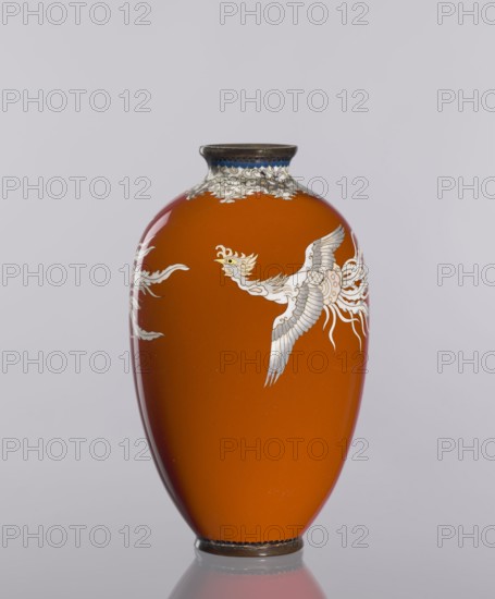 Vase, cloisonné enamel, ca. 1910–1920 Meiji/Taisho periods, Japan. Vessel with phoenixes and plant ornaments on a dark brick-red background; height 12.8 cm, diameter 7.7 cm., A smooth, glossy orange vase with a narrow dark rim and base features a decorative white bird motif with light gray and pale yellow details and flowing white accents against a plain pale gray background.