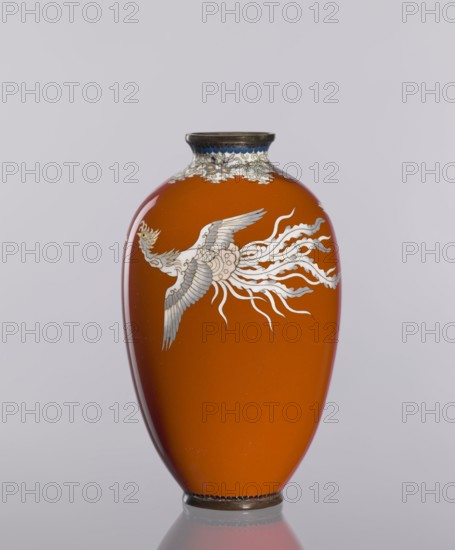 Vase, ; Japanese, ca. 1910–1920 Meiji/Taisho periods; cloisonné enamel vessel, height 12.8 cm, diameter 7.7 cm; decorative vase with phoenixes and plant ornaments on a dark brick-red background., An oval vase with a glossy orange body sits against a pale gray background, decorated with a stylized bird motif in white and gray with flowing, ribbon-like tail elements; the bird has feather details and a crest, and there is a decorative band around the narrow neck in shades of white, blue, and gray with metallic accents; the vase has a dark metallic rim at the top and bottom and a subtle reflection beneath it.