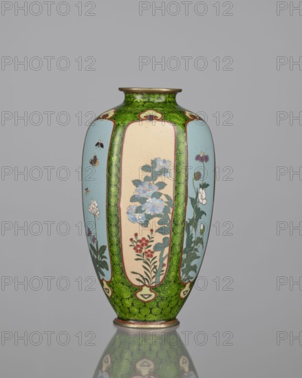 Vase, cloisonné enamel, floral pattern with butterflies and dense green floral rosettes in reserved background, Meiji period 1868–1912, Japan, 19th/20th century; vessel; height 15.3 cm, width 8.7 cm, depth 8.2 cm., A tall decorative vase with a rounded body and narrow neck sits against a plain gray background, showing a glossy surface with a reflective base. The vase features a dominant green background mottled with darker green patterning, interrupted by a few vertical panels in pale blue and cream. Within the cream and blue panels are painted botanical motifs including clusters of flowers and leaves in colors such as light blue, red, purple, white, and various greens, along with a few small insects depicted in dark brown and black. The rim and base have thin metallic bands in a muted gold color. The overall palette includes green, pale blue, cream, light blue, red, purple, white, dark brown, black, and muted gold.