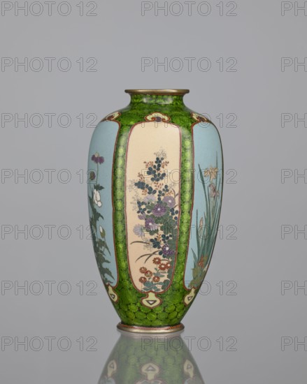 Vase, cloisonné enamel, floral pattern with butterflies and plant ornaments, Meiji period 1868–1912, Japan, 19th/20th century. Background of decoration in reserves: dense green floral rosettes and butterflies. Vessel; height 15.3 cm, width 8.7 cm, depth 8.2 cm.,  noted., A tall, rounded vase with a narrow neck and flared rim stands upright against a plain gray background. The vase features a bright green base color with a textured, mottled pattern covering much of its surface, and several vertical panels in pale blue and cream that display detailed floral designs. The floral panels show clusters of flowers and stems in colors including purple, pink, blue, white, and muted red, with green leaves and slender grasslike foliage. The rim and foot have metallic accents in a bronze or gold tone, and a subtle reflection of the vase appears on the smooth surface beneath it.