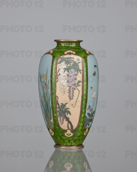 Vase, cloisonné enamel, floral pattern with butterflies and plant ornaments; background of decoration in reserves: dense green floral rosettes and butterflies. Japanese, Meiji period 1868–1912, 19th/20th century. Vessel. Height 15.3 cm, width 8.7 cm, depth 8.2 cm., A tall, narrow vase with a rounded body and a slightly flared neck standing on a reflective surface, decorated with panels framed by a textured green background; the vase shows painted floral scenes in muted tones including light blue, pale beige, purple, white, green, and touches of brown and gold, with leafy branches, hanging blossoms, slender stems, and small insects depicted within the panels, and the green area showing a mottled pattern that continues down to a decorative base ring.