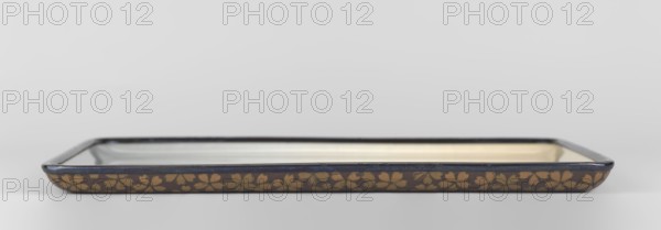 Tray by Namikawa Sôsuke 1847–1910. Rectangular tray with rounded corners decorated on the obverse with an asymmetrical composition showing a white heron standing on one leg, the other hidden in feathers, next to a clump of white and blue irises. The background is neutral, ranging from bluish at the bottom to cream at the top, with a slight hint of pink, suggesting the delicate, fading glow of the aurora. The entire composition is in a painterly style, achieved using the musen technique enamel without wires. Sparse wires shosen technique define a few details — the bird's beak and legs. The reverse is covered with a dense cherry blossom ornament in two shades of brown against a uniform matte dark brown enamel; the flowers are executed using the cloisonné technique yusen with gold wires, and in the center is a silver-wired seal woven with the signature Sakigake. Deep glossy black metal tray edge made of shakudo alloy. Ca. 1890–1900 Meiji period, Nagoya, Japan. Vessel: height 1.3 cm; width...