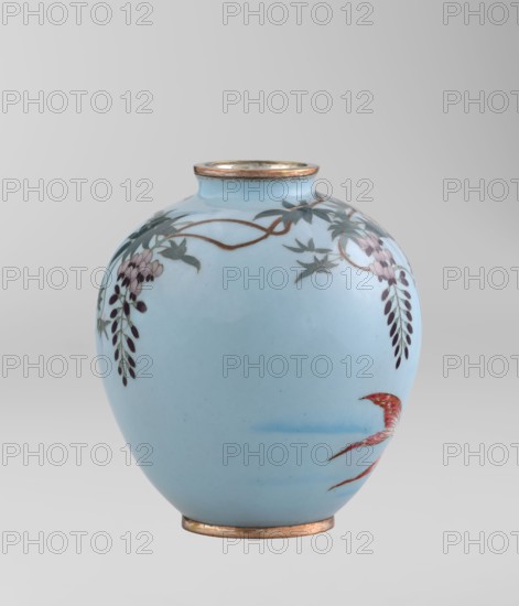 Vase, Gonda Hirosuke 1865–1937 maker. Small spherical cloisonné enamel vase, one of a pair, on a low ring foot and a round ring spout, both set in silver-plated metal. Decorated with a realistic, colorful motif of red veil fish beneath hanging wisteria leaves and flowers on a light blue background. The bottom bears a brand in the form of a flaming pearl with the character yu written in katakana — the mark of enameller Gonda Hirosuke of Nagoya. Circa 1890–1910 Meiji 23–43, Nagoya, Japan. Height 9.0 cm; diameter 8.2 cm., A pale blue rounded ceramic vase with a narrow rim and base finished in a metallic warm tone, decorated with trailing floral motifs in shades of purple, green, and brown and a small stylized red and pink bird-like form near the lower side, all set against a light gray gradient background.