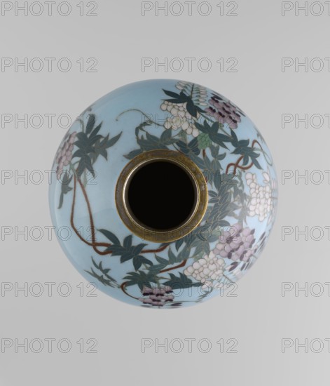 Vase, Gonda Hirosuke 1865–1937 maker. Small spherical cloisonné enamel vase, one of a pair, on a low ring foot and a round ring spout, both set in silver-plated metal. Decorated with a realistic colorful motif of red veil fish beneath hanging wisteria leaves and flowers on a light blue background. The bottom bears a brand in the form of a flaming pearl with the character yu in katakana — the mark of enameller Gonda Hirosuke of Nagoya. Circa 1890–1910 Meiji 23–43, Nagoya, Japan. Height 9.0 cm; diameter 8.2 cm., A rounded ceramic vessel viewed from above with a central opening rimmed in aged metallic gold, the body glazed in pale blue and decorated with a flowing pattern of dark green leaves, brown winding stems, and clusters of small rounded blossoms in shades of white and pale purple.