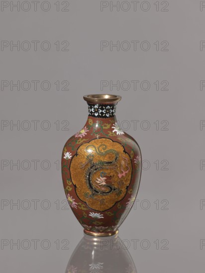 Vase, repossession; phoenixes iconography, Japanese art, lotuses, dragons iconography, Japanese culture, Meiji 1868–1912, hoo phoenix, birds, cloisonné enamel, ca. 1900–1910 Meiji Period, Japan, Kyoto, vessel, height 12.3 cm, diameter 7.2 cm, A glossy vase with a rounded body and narrow neck sits against a plain gray background, the main surface showing a rich reddish-brown color with decorative green scrolling and floral motifs in white, pink, and yellow, a central golden oval panel on the body containing a stylized serpentine creature rendered in darker tones with accents of blue and pink, the neck bordered by a band with black and white floral patterns and a metallic gold rim at the mouth and base, and the vase casting a subtle reflection on the surface beneath it.