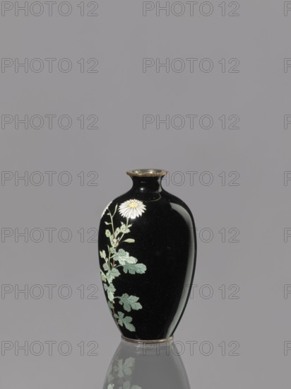 Vase, chrysanthemums, cloisonné enamel, ovoid elongated vase, Meiji period 1868–1912, Japan, 19th/20th century, height 9.0 cm, diameter 5.3 cm., A glossy black vase with a narrow neck and flared rim stands centered against a gray background, decorated on one side with a painted pale yellow and white flower and a stem with several green leaves, and its reflection appears faintly below on a reflective surface; visible colors include black, gray, pale yellow, white, light green, and a hint of gold on the rim.