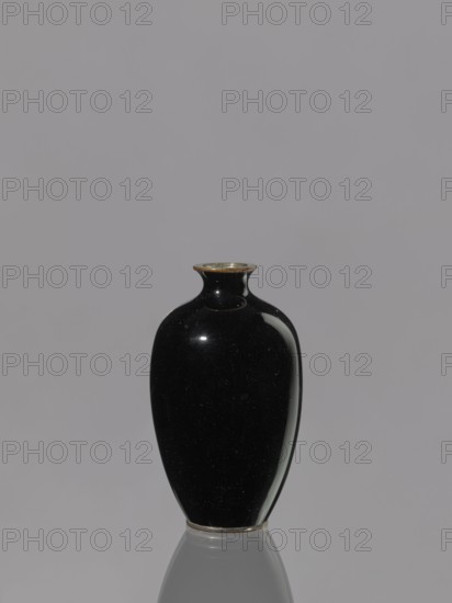 Vase, chrysanthemums, Japanese art, Japanese culture, flowers iconography, Meiji 1868–1912, cloisonné enamel, ovoid elongated vase, 19th/20th century Meiji period, 1868–1912, Japan; vessel; height 9.0 cm, diameter 5.3 cm, A glossy black vase with a rounded, elongated shape and a narrow neck sits centered against a smooth light gray background, its rim showing a thin metallic edge in a bronze tone and its base resting on a reflective surface that creates a faint mirror image; highlights on the vase show subtle white reflections and the overall scene includes colors of black, light gray, white, and a touch of bronze.