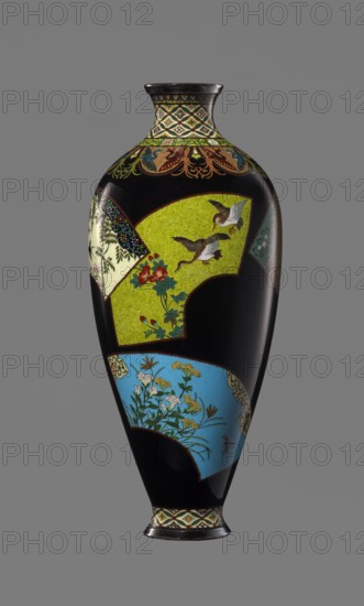Vase by Namikawa Yasuyuki 1845–1927, cloisonné enamel, ca. 1890–1905 Meiji period. Small, slender vase tapering toward the bottom to a ring-shaped silver foot; short neck with a slightly parted spout enclosed by a silver ring. Ornamental shippo cloisonné border with rosettes in rhomboid fields at the foot and neck. Petal decoration filled with stylized phoenix images flows down to the shoulders. Belly finished in glossy black enamel with six colorful, fan-shaped reserves depicting various floral and bird motifs, executed with meticulous precision in the yusen technique with silver wires. Silver plaque mounted in the mirror of the base engraved “Kyoto Namikawa.” Height 18.0 cm; diameter 7.8 cm., A tall, narrow vase with a glossy black background features several fan-shaped painted panels in bright colors and ornate borders; a large lime green panel shows two flying birds with brown and white feathers above a branch with red and green flowers, a sky-blue panel displays delicate white and...