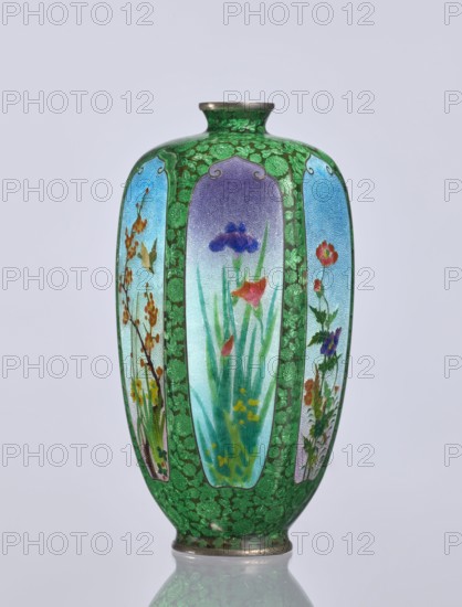 Vase, gift, repossession Krakow — elongated hexagonal cloisonné enamel vase with a narrow spout. Decoration: small, densely spaced floral rosettes and butterflies on a black background; additional motifs include flowers, irises, and birds. Japanese, Meiji period 1868–1912, 19th/20th century. Vessel. Height 12.5 cm, width 6.7 cm, depth 6.1 cm., A tall vase with a rounded body and narrow neck, decorated with a green background patterned with darker green clover-like shapes and bordered panels showing painted floral scenes; the panels contain flowers and foliage in colors including purple, blue, red, orange, yellow, pink, and various greens set against pale blue to lavender backgrounds, and the vase has metallic rims at the top and base with reflections visible on the smooth surface.