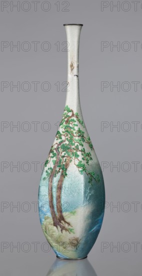Vase, Kawaguchi Bunzaemon 1860–post 1910, craftsman. Slender cloisonné enamel vase with a long thin neck. Decoration: two pine trees growing on a seaside rock, the rolling sea and two flying cranes. Meiji period, late 19th century 1868–1912. Japan, Nagoya. Vessel; height 30.6 cm, width 7.8 cm. Gift; revindication noted., A tall, slender vase with a narrow neck and flared rim stands against a gray background, the surface showing a textured, pale off-white finish near the top that transitions into soft aqua and blue tones toward the base; a painted scene decorates the body featuring a group of brown tree trunks with green foliage, branches extending outward over a landscape that includes muted greens and sandy beige at the roots and hints of blue suggesting water, with subtle darker and lighter shading across the form.