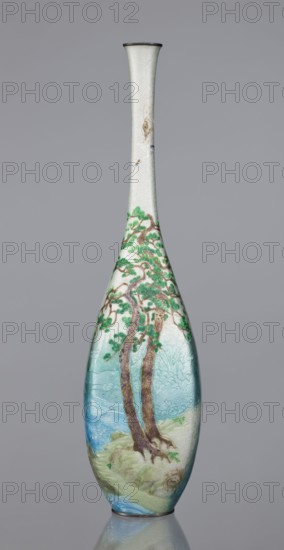 Vase by Kawaguchi Bunzaemon 1860–post 1910, craftsman. Slender cloisonné enamel vase with a long thin neck. Decoration: two pine trees growing on a seaside rock, the rolling sea and two flying cranes, seas, waves, clouds. Meiji period, late 19th century 1868–1912. Japan, Nagoya. Vessel. Height 30.6 cm; width 7.8 cm., A tall, slender vase with a narrow neck and flared rim stands against a plain gray background; the vase surface shows a textured, pale off-white area near the neck transitioning into a painted scene of a group of trees with brown trunks and green foliage set against bluish-green and pale turquoise areas that suggest water and land, with additional muted greens and light browns in the lower portion and a darker rim at the top.