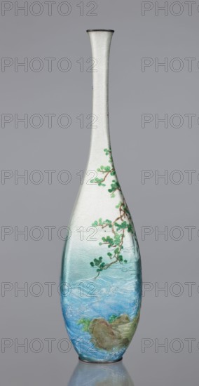 Vase by Kawaguchi Bunzaemon 1860–post 1910, maker craftsman. Cloisonné enamel vase, Meiji period, late 19th century 1868–1912. Slender vessel with a long, thin neck, height 30.6 cm, width 7.8 cm. Decoration: two pine trees growing on a seaside rock, the rolling sea and two flying cranes. Japan, Nagoya., A tall, slender vase with a narrow neck and a flared rim stands against a plain gray background, its surface textured and primarily off-white toward the top, transitioning into soft aqua and deeper blue tones toward the base; a delicate painted branch with green foliage climbs the upper portion, while the lower area shows stylized flowing water in shades of blue with subtle white highlights and a few greenish-brown rocks and vegetation near the base.
