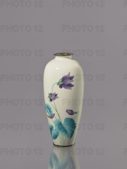 Vase, Taisho period, ca. 1912–1926. Japan, Nagoya. Cloisonné enamel. Vessel with narrow rim, height 15.1 cm, width 6.6 cm. Decoration: a tuft of blooming lilac bellflowers along almost the entire height of the belly. Iconography: flowers; Japanese., A smooth, cream-colored ceramic vase with a narrow neck and rounded shoulders stands upright against a muted gray background, decorated with a botanical motif featuring purple bell-shaped flowers and teal-green leaves and stems, with a metallic rim at the top and a metallic band at the base, and the vase's lower portion and design reflected faintly on the glossy surface beneath it.